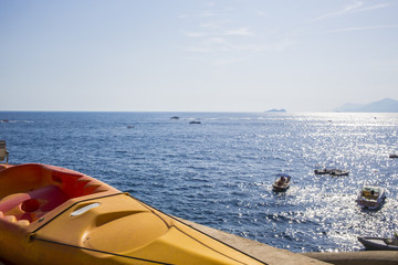 Dettaglio di una canoa gialla monoposto ferma sulla spiaggia. Nel mare gommoni, barche e moto d'acqua sfrecciano verso l'orizzonte dove si intravede l'isola di Capri.