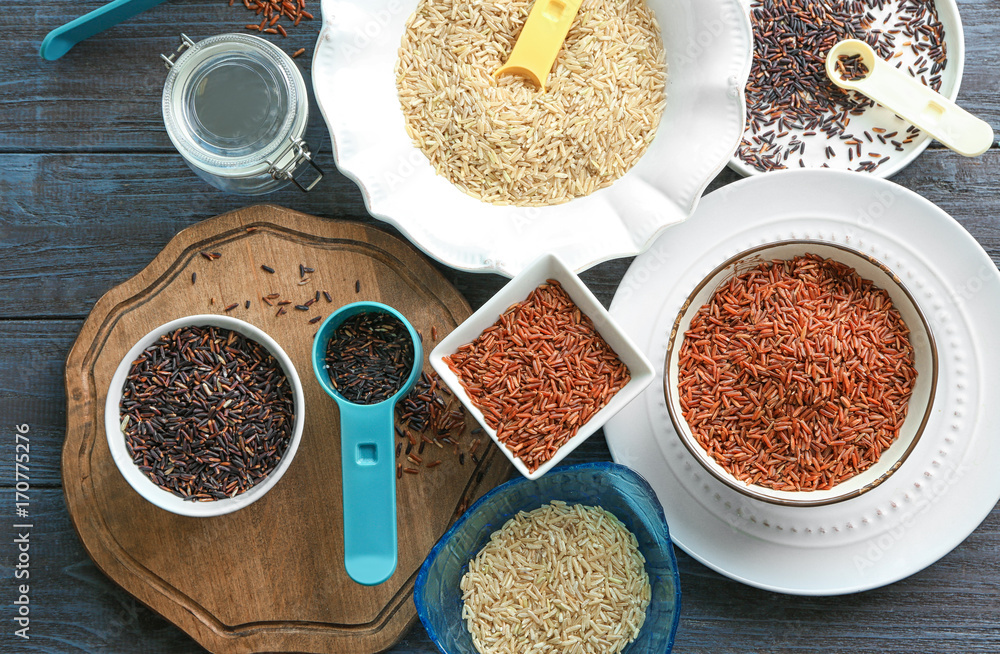 Different types of rice in bowls and plates on wooden table