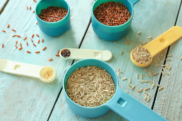 Canvas Print - Different types of rice in  measuring scoops on wooden table