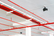 Fire sprinkler system with red pipes is placed to hanging from the ceiling inside of an unfinished new building.