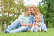 © serhiibobyk - Beautiful loving couple cuddling while sitting on the grass together with their little daughter copyspace love family parenthood affection children parenting leisure holidays weekend concept.