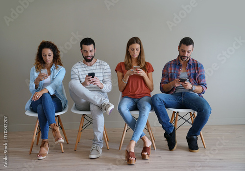 Young People In Waiting Room Looking At Smartphone Kaufen