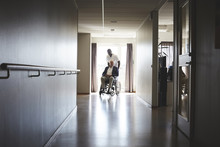 Full Length Of Male Nurse Pushing Senior Man On Wheelchair At Hospital Corridor