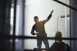 © Maskot - Businesswoman looking at male professional giving presentation against wall in board room seen from glass at creative of