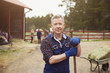 © Maskot - Portrait of confident farmer holding pitchfork while standing in farm