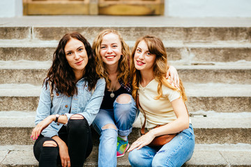 cute group of three teenages girl sitting on the stairs of the university building huggings, smiling