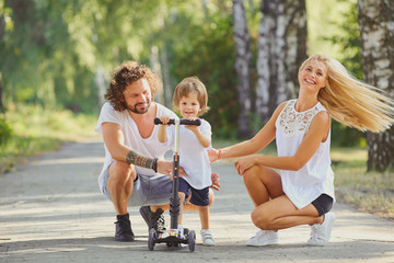 Happy family in the park. Parents with a child on a scooter are walking in nature.