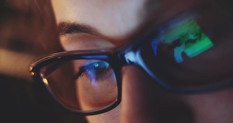 Reflection of a Tablet Computer Screen in Woman Glasses at Night. SLOW MOTION 4K DCi, Dolly Shot. Woman using digital tablet, browsing internet, watching movie. Light reflections in glasses.