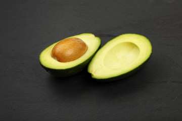 Two halves of avocado on black slate board