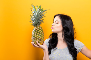 Wall Mural - Happy young woman holding a pineapple on a yellow background