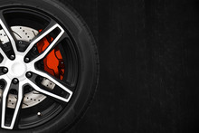 Alloy Wheels Of Racing Car With Metal Brake Discs And Red Caliper On A Black Cement Wall Background With Copy Space Your Writing Text On The Right. Automotive Parts Concept.