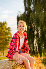 Young girl on straw sheaves in a field