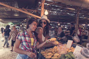 Wall Mural - Young Women Talking While Buy Exotic Fruits On Tropical Market Happy Smiling Girld Tourists Choosing Products In Asian Traditional Bazaar