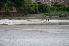 Surfers Ride The Severn Bore Tidal Wave At Newnham-on-Severn, Gloucestershire