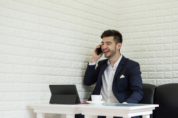 Young businessman using smartphone while working on his laptop in office.