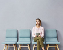 Portrait Of Confident Serious Young European Female Sitting On Chair In Waiting Room With Electronic Tablet, Setting Her Mind Up Before Job Interview Or Meeting With Potential Business Partners