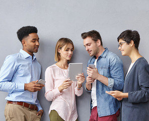 Candid shot of talented creative young men and women business partners having discussion on startup project, developing successful strategy and business plan, using gadgets. Teamwork and cooperation