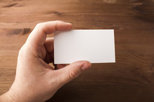 Blank Business Card In Hand On A Wooden Background. For Your Design. Model For Brand Identification