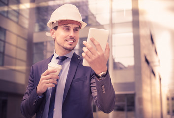 Smiling architect in helmet working at touchpad