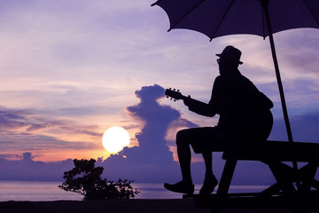 Man playing guitar on the beach with sunrise