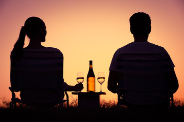 Wall Mural - Couple watching the sunset enjoying a glass of wine. 