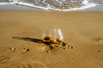 two glasses of whiskey single malt on the sand washed by the waves, a glass of tasting, relax on the beach