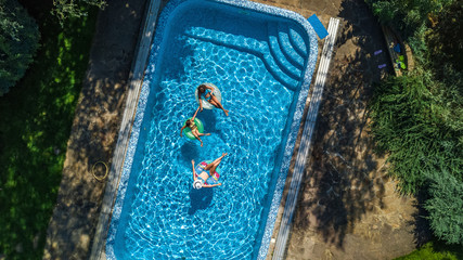 Wall Mural - Aerial top view of family in swimming pool from above, happy mother and kids swim on inflatable ring donuts and have fun in water on family vacation
