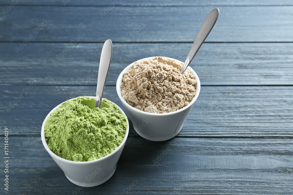 Bowls with protein and barley grass powder on wooden background