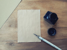 Blank Old Sheet Of Paper With A Dip Pen, An Inkwell And An Envelope On A Worn Wooden Background (view From The Top Or Flat Lay), Retro Style