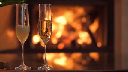 Wall Mural - Champagne in two glasses on table in front of burning fireplace.