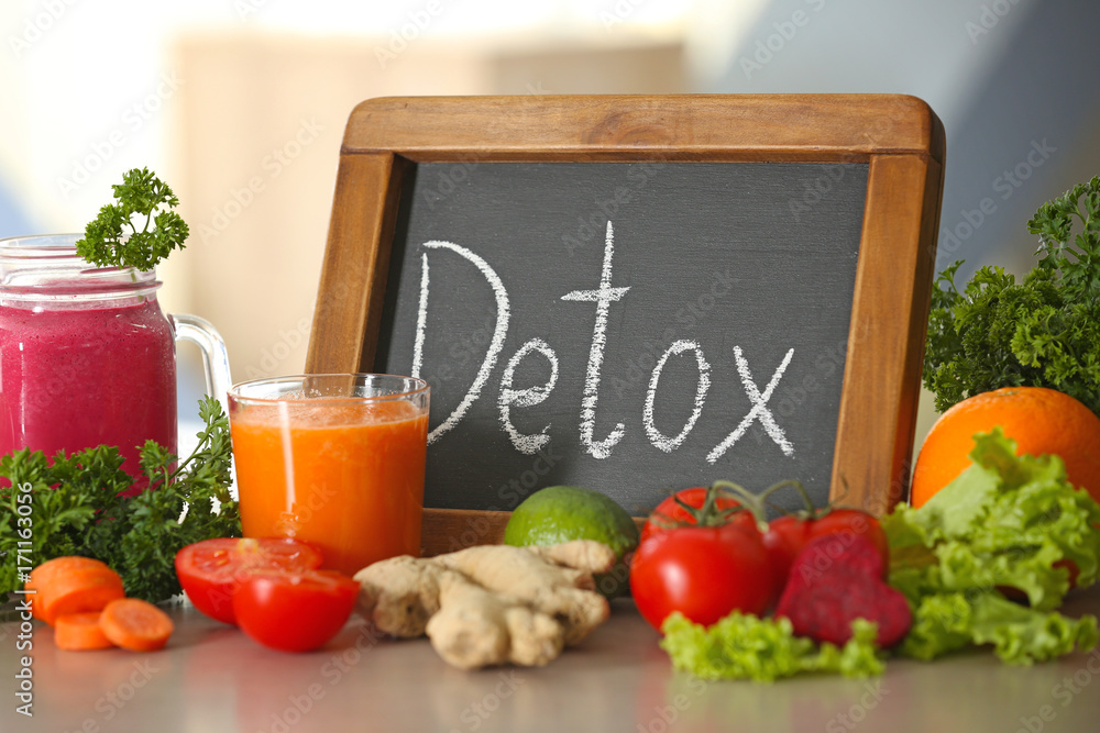 Small chalkboard with word DETOX, fresh juices and ingredients on table