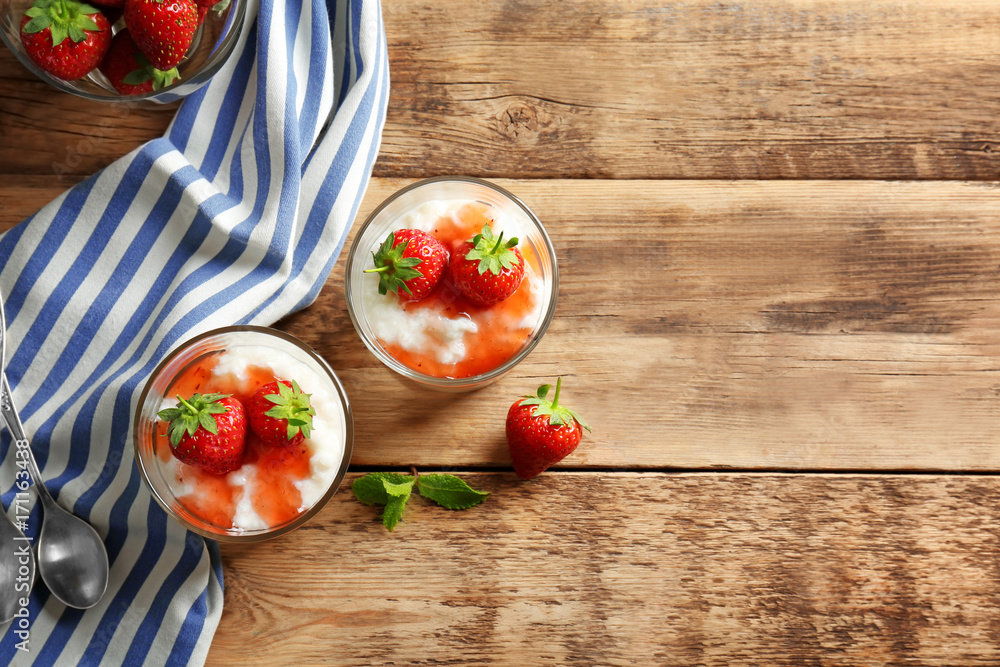 Creamy rice pudding with strawberry in glasses on wooden table