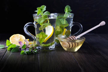 Two glass cups fresh mint tea with lemon and honey on dark background.