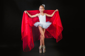 Little young ballerina posing with red cloth in hands on a black background.