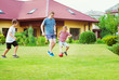 © spass - Two happy sons playing football with their father in garden near House