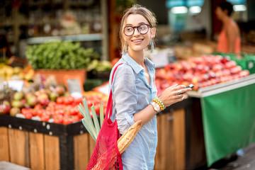 Wall Mural - Young woman using smartphone standing with bag in front of the food market in France