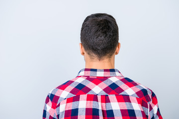 Rear view photo of young brunet hipster with modern haircut, in a checkered shirt, standing isolated on gray background