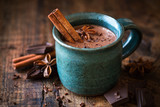 Hot chocolate with a cinnamon stick, anise star and grated chocolate topping in festive Christmas setting on dark rustic wooden background