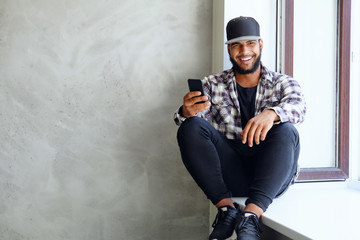 A black male sits near window and using a smartphone.