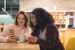 © Wavebreak Media - Female friends using mobile phone in café
