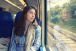 © papa - The young woman sadly looking out the window sitting inside the train car.