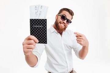 Sticker - Happy young bearded man holding passport and tickets while pointing.