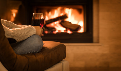 Young woman sitting at home by the fireplace and drinking a red wine.