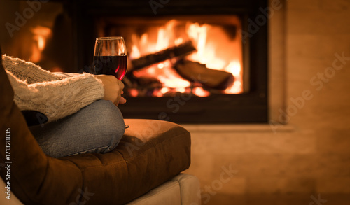 Fotografía Young woman sitting at home by the fireplace and drinking a red wine