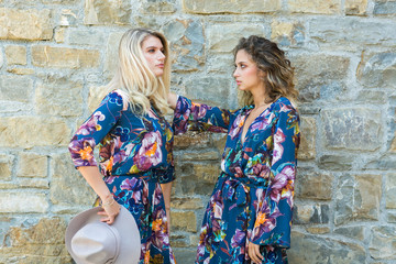 Fashion portrait of two happy woman with blue eyes in flower dress. Fashion hat in a sunny day. Girl with long blonde healthy hair and beautiful smile.