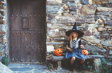 Little Girl In Witch Costume Sitting On Bench