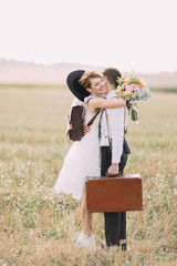 The lovely side portrait of the happy vintage dress newlyweds hugging in the sunny field.