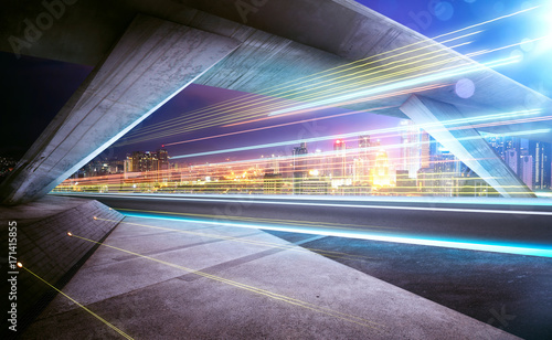 Fototapeta na szkło Empty asphalt road under the bridge during the night with light trails and beautiful city skyline background .