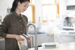 © amanaimages - Woman wiping glass in kitchen