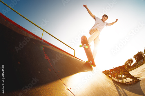 Fotografia Teen skater hang up over a ramp on a skateboard in a skate park